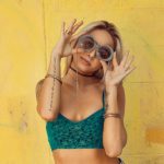 Sustainable Model - woman in blue bralette holding sunglasses putting on her eyes