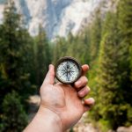 Ethical Compass - person holding compass facing towards green pine trees