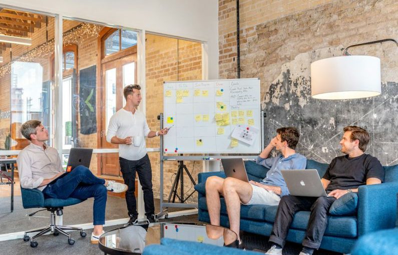 Inspiring Leaders - three men sitting while using laptops and watching man beside whiteboard