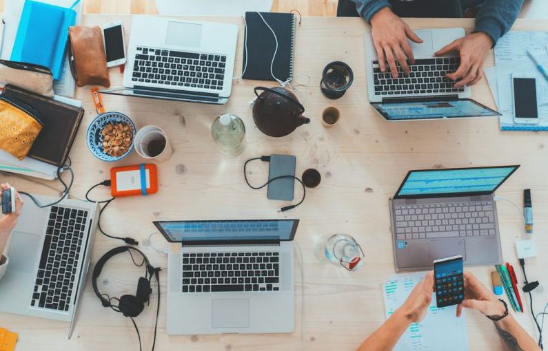 Technology Impact - people sitting down near table with assorted laptop computers