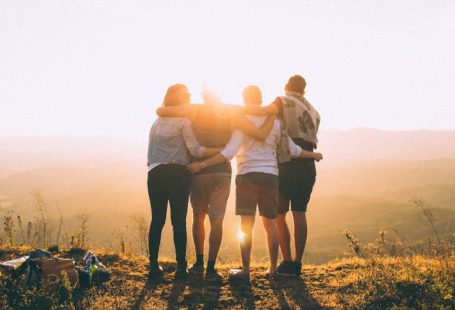 Community Impact - four person hands wrap around shoulders while looking at sunset