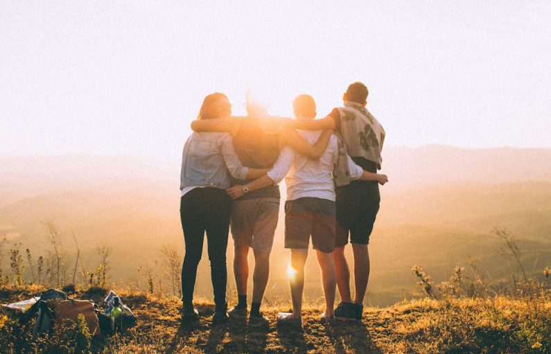Community Impact - four person hands wrap around shoulders while looking at sunset